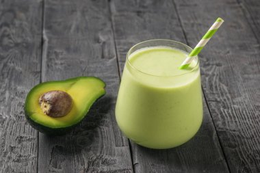 Yarım avokado, buzlu cam bardak ve ahşap bir masada kokteyl tüpü. Fitness ürünü.