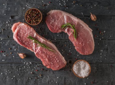 Two pork steaks with spices and coarse salt on a wooden table. The view from the top.