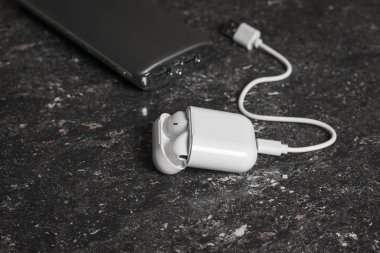 Taştan bir arka planda beyaz kablosuz kulaklıklar ve elektrik bankası.