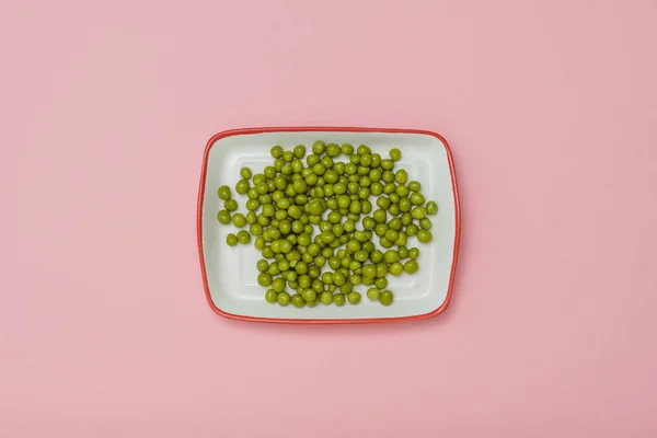 Placa rectangular blanca con guisantes verdes sobre fondo rosa . — Foto de Stock