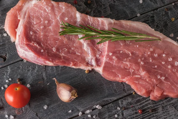 Tomato, garlic, rosemary and a large piece of meat on a wooden table. — Stock fotografie