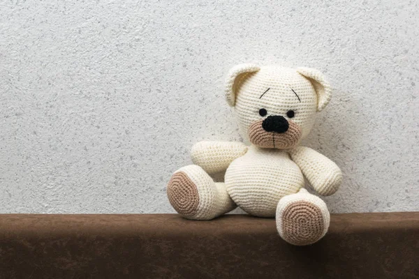 Knitted polar bear with brown paws on the sofa against the wall.