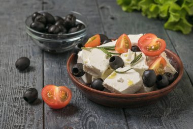Pieces of feta cheese with olives and tomatoes in a clay bowl.