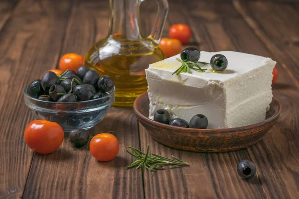 A large piece of feta cheese in a clay bowl with olives and tomatoes on a wooden table. — Stock Photo, Image