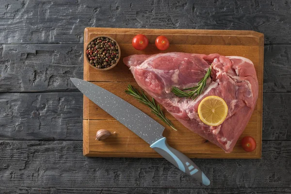 Egy nagy darab sertéshús, egy kés, paradicsom és fokhagyma a vágódeszkán. A kilátás felülről. — Stock Fotó