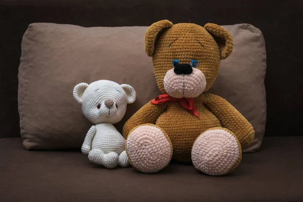 A large knitted bear hugs a small one on a brown sofa.
