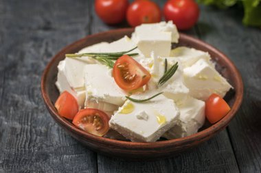 Tahta bir masada, kil bir kasede beyaz peynir dilimlenmiş kiraz domatesleri..