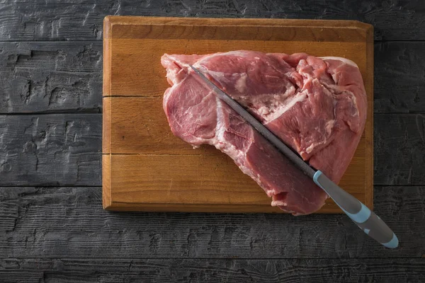 Uma faca com uma alça azul corta um grande pedaço fresco de porco. A vista de cima . — Fotografia de Stock