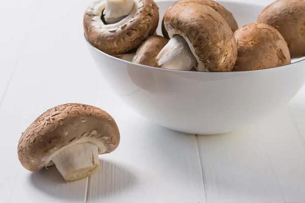 Large mushrooms of the Royal variety in a white bowl on a white wooden table. Vegetarian food. — Stockfoto