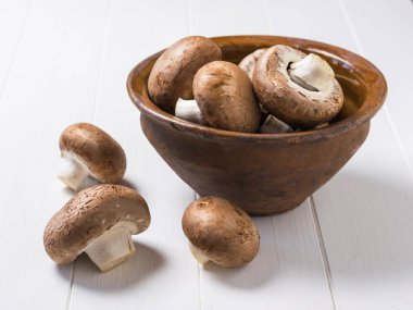 Royal mushrooms in a clay bowl and on a white wooden table. Vegetarian food.