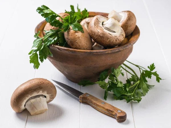 Königliche Pilze in einer Tonschüssel, ein Messer und Petersilienblätter auf einem weißen Holztisch. Vegetarisches Essen. — Stockfoto