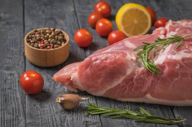 Ahşap bir masada büyük bir et parçasının yanında kiraz domates ve baharatlar..