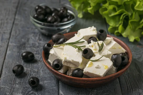 Feuilles de laitue et un bol de fromage feta et d'olives sur une table en bois noir . — Photo