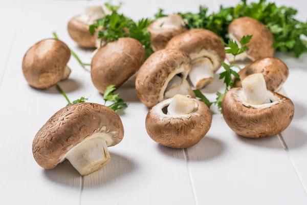 Petersilienblätter und Königspilze verstreut auf einem weißen Holztisch. Vegetarisches Essen. — Stockfoto