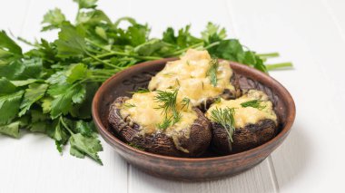 A bunch of parsley leaves and three Royal baked mushrooms on a white table.