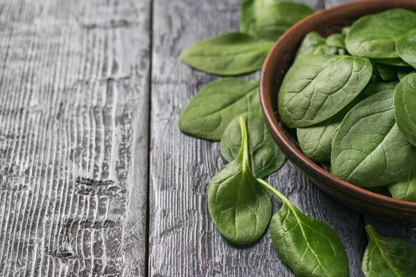Spinach leaves and a clay bowl on a black rustic table. Food for fitness. — Stockfoto