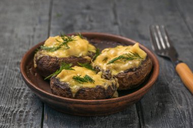 Fork next to a clay bowl with three baked mushrooms.