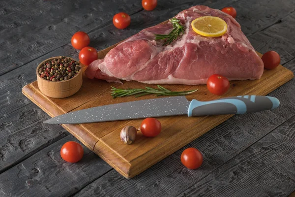 Um pedaço de carne com especiarias e uma faca com uma alça azul na tábua de corte . — Fotografia de Stock