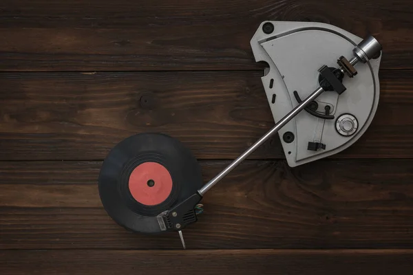 Un grabador de vinilo y un disco rojo sobre una mesa de madera . — Foto de Stock