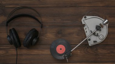 Tahta bir arka planda kırmızı vinil disk ve kulaklık çalan klasik bir oyuncu.