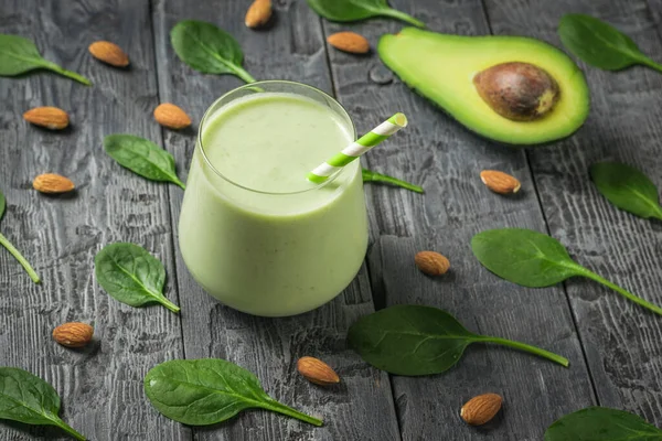 Avocado, spinach leaves, almonds, and a glass of smoothies on a black wooden table. Fitness product.