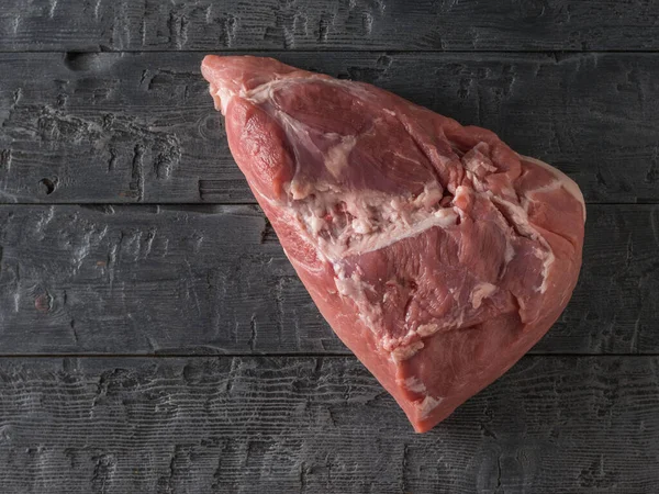 Um grande pedaço de carne fresca de porco em uma mesa rústica preta. A vista de cima . — Fotografia de Stock