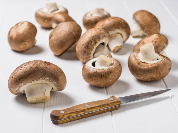 Ein Messer mit Holzgriff und große Royal Pilze auf dem Tisch verstreut. Vegetarisches Essen. — Stockfoto