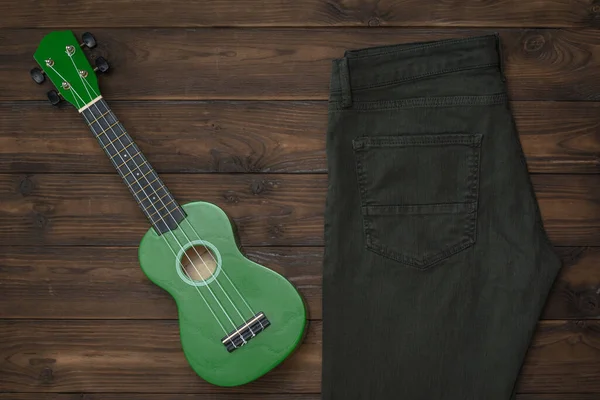 Зеленые джинсы и зеленая укулеле на деревянном фоне . — стоковое фото