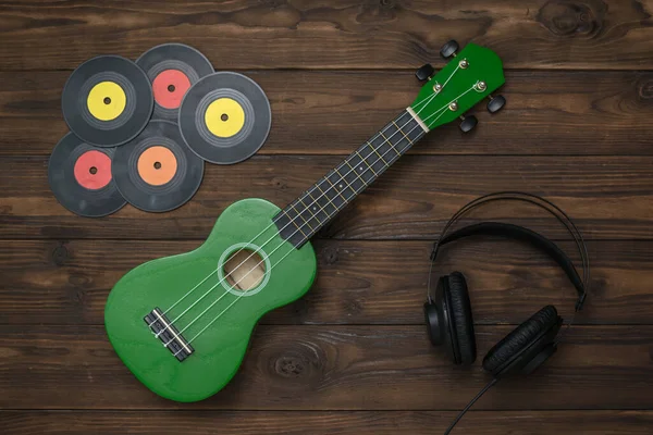 Зеленая укулеле, пять виниловых дисков и наушники на деревянном фоне . — стоковое фото