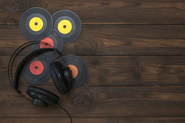 Headphones and colorful vinyl discs on a wooden background.