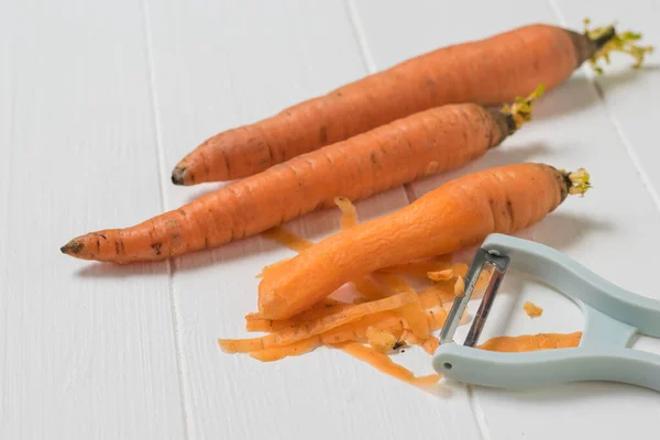 Три морковки и кожура на белом деревянном столе . — стоковое фото