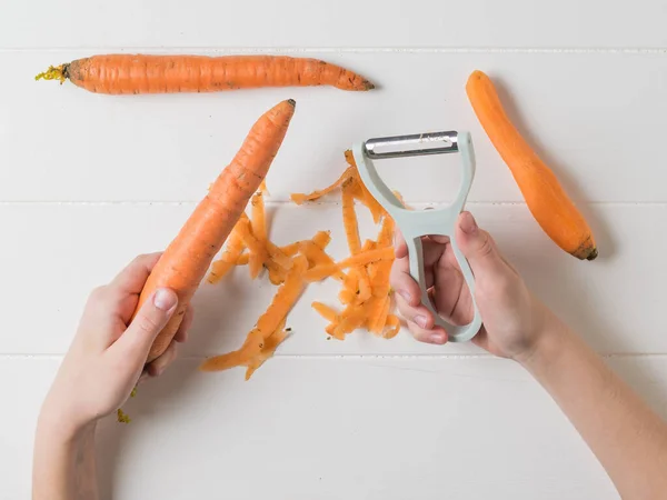 बच्चे एक सब्जी पिलर के साथ गाजर की सफाई में लगे हुए हैं . — स्टॉक फ़ोटो, इमेज