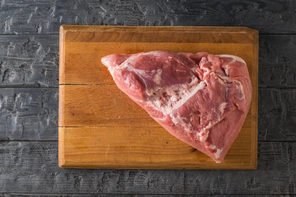 Tabla de cortar de madera con un pedazo grande de cerdo en una mesa de madera. La vista desde arriba . —  Fotos de Stock