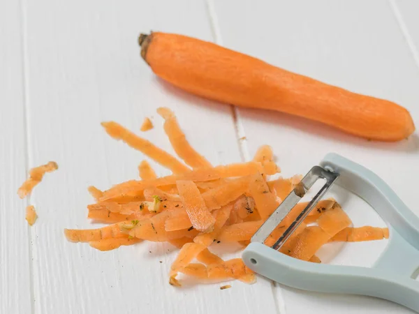 Очищенная морковь и чистящие средства на белом деревянном столе . — стоковое фото