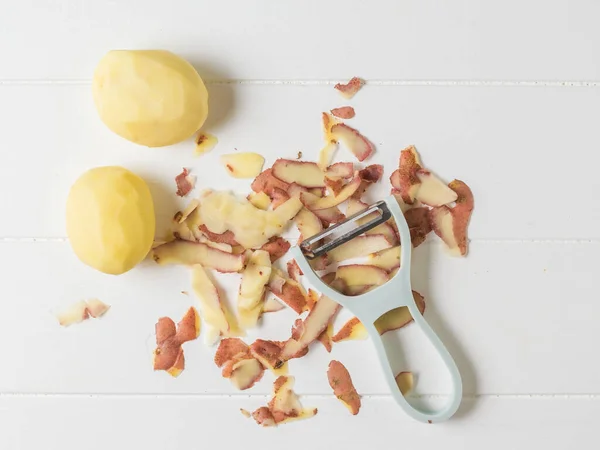 Dos papas peladas y un dispositivo de despiece en una mesa de madera blanca . — Foto de Stock