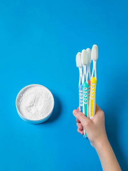 Set of silicone toothbrushes in hand and tooth powder on a blue background. — Stock Photo, Image