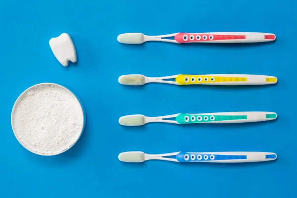 A set of toothbrushes with silicone bristles, tooth powder and a tooth figurine on a blue background. — Stock Photo, Image