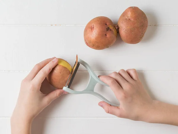 Фруктовая картошка и руки чистят картошку на деревянном столе . — стоковое фото