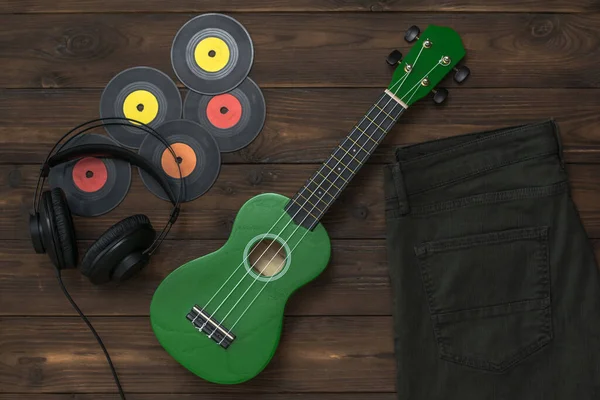 Зеленая укулеле, наушники, виниловые диски и джинсы на деревянном фоне . — стоковое фото