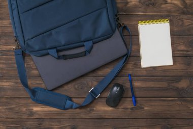 Üzerinde çıkıntılı bir dizüstü bilgisayar, bir fare ve tahta bir defter olan mavi bir çanta.. 