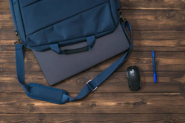 Mavi kalem, fare ve dizüstü bilgisayar ve tahta arka planda bir çanta..