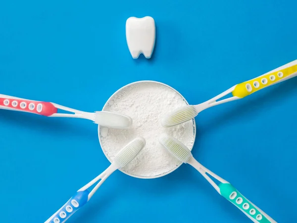 Tooth powder, four silicone toothbrushes, and a tooth figurine on a blue background. — Stock Photo, Image