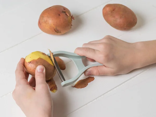 Fata cojește cartofii cu un cuțit special gri . — Fotografie, imagine de stoc