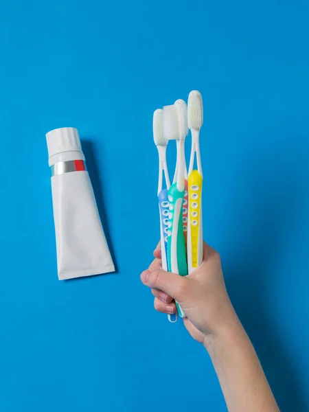 A hand with silicone-bristled toothbrushes and a tube of toothpaste on a blue background. — Stock Photo, Image