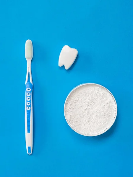 A tooth figurine, a blue toothbrush, and a jar of tooth powder on a blue background. — Stock Photo, Image