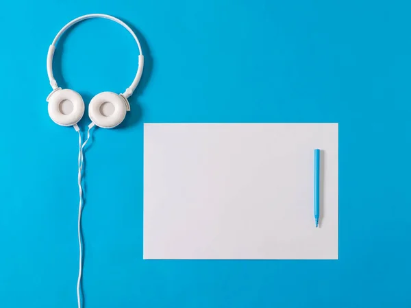 Weiße Kopfhörer, ein weißes Blatt Papier und ein blauer Marker auf blauem Hintergrund. — Stockfoto