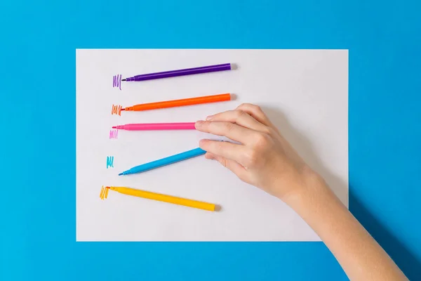 Het kind probeert verschillende kleuren markers op wit papier. — Stockfoto