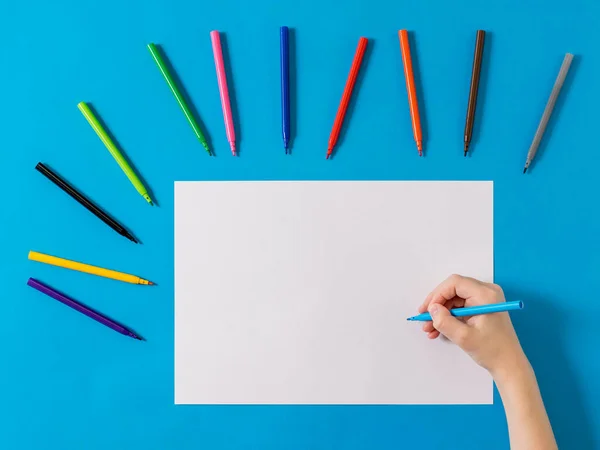 Een hand met een blauwe stift op een wit laken en een set stiften op een blauwe achtergrond. — Stockfoto