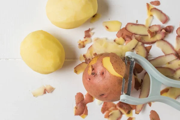 Pelador que corta la capa superior de papas sobre una mesa blanca . — Foto de Stock