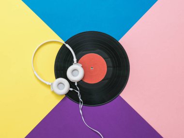Kablolu beyaz kulaklıklar ve çok renkli bir arka planda vinil disk..